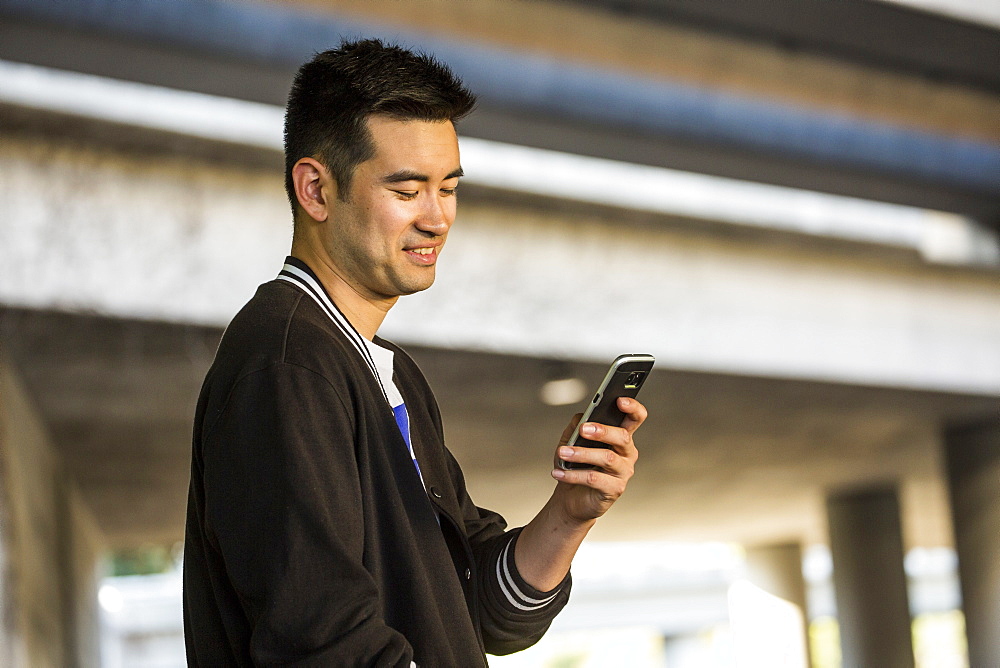 Smiling Chinese man texting on cell phone