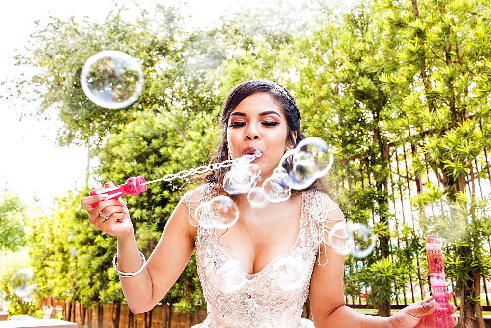 Hispanic girl wearing gown blowing bubbles