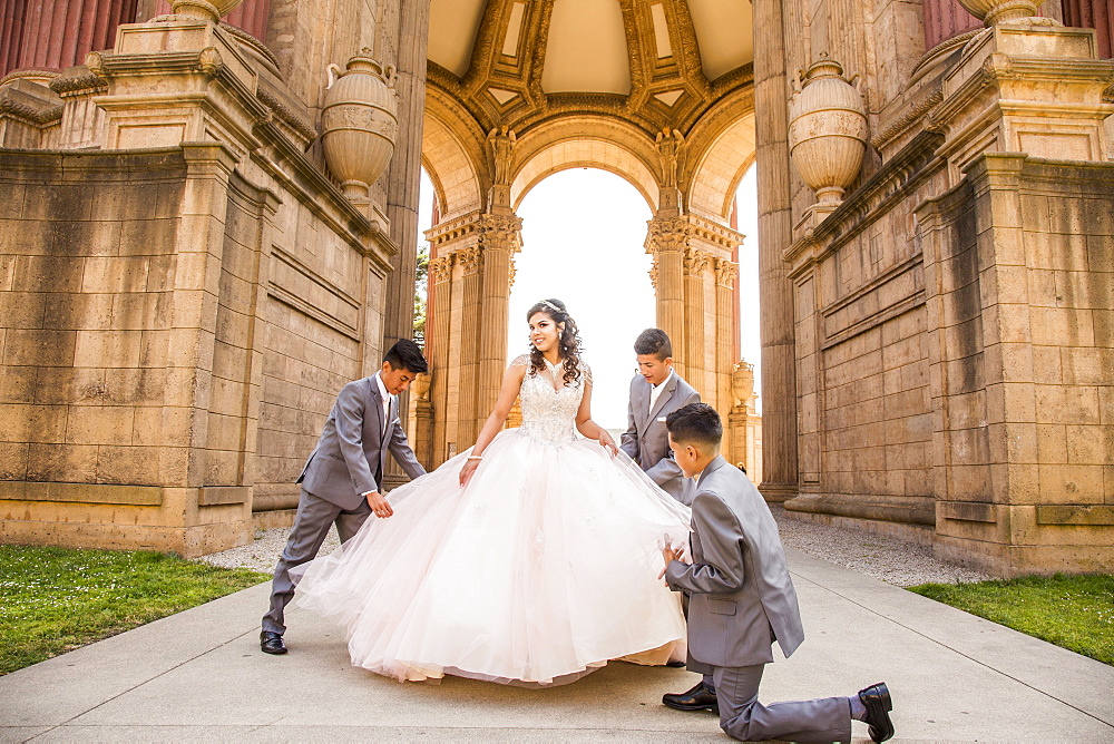 Hispanic boys holding skirt of girl