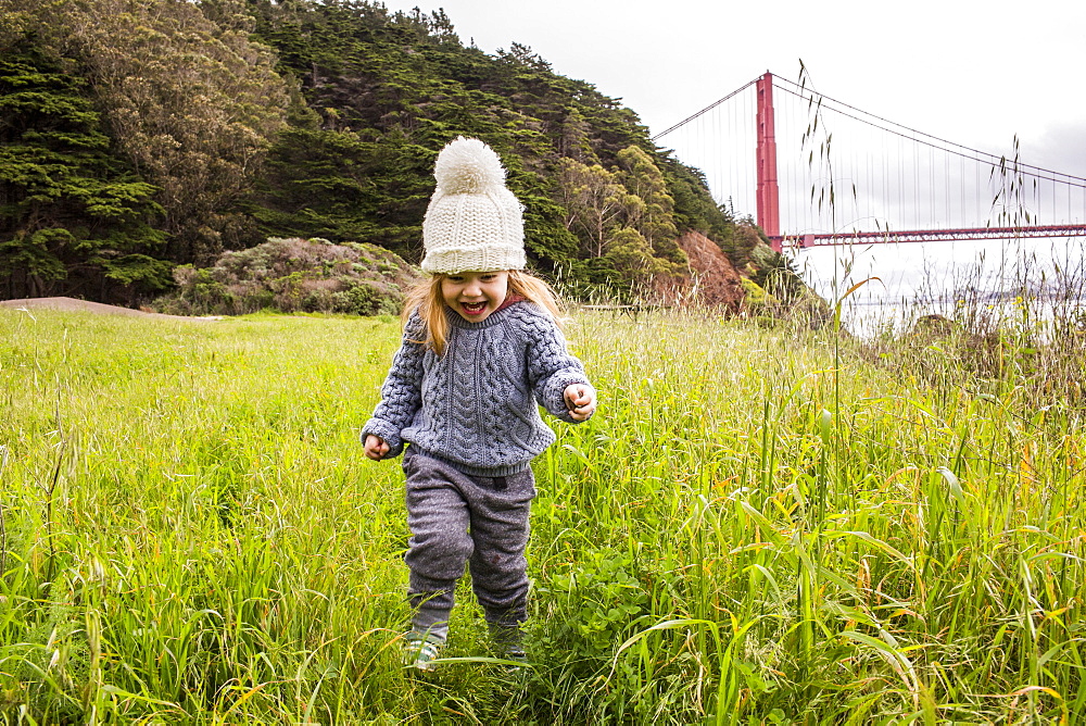 Caucasian girl running in grass near bridge