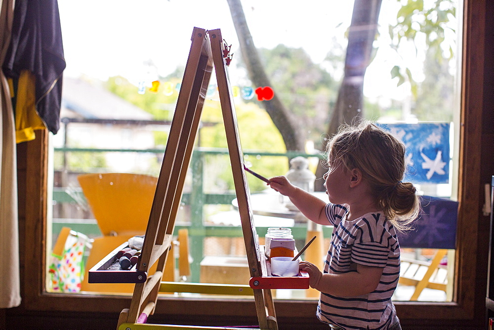 Caucasian girl painting on easel near window