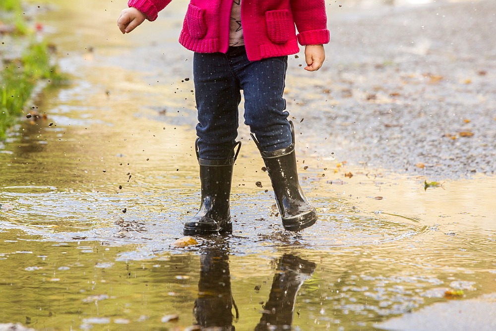 Caucasian girl wearing boots splashing in puddle