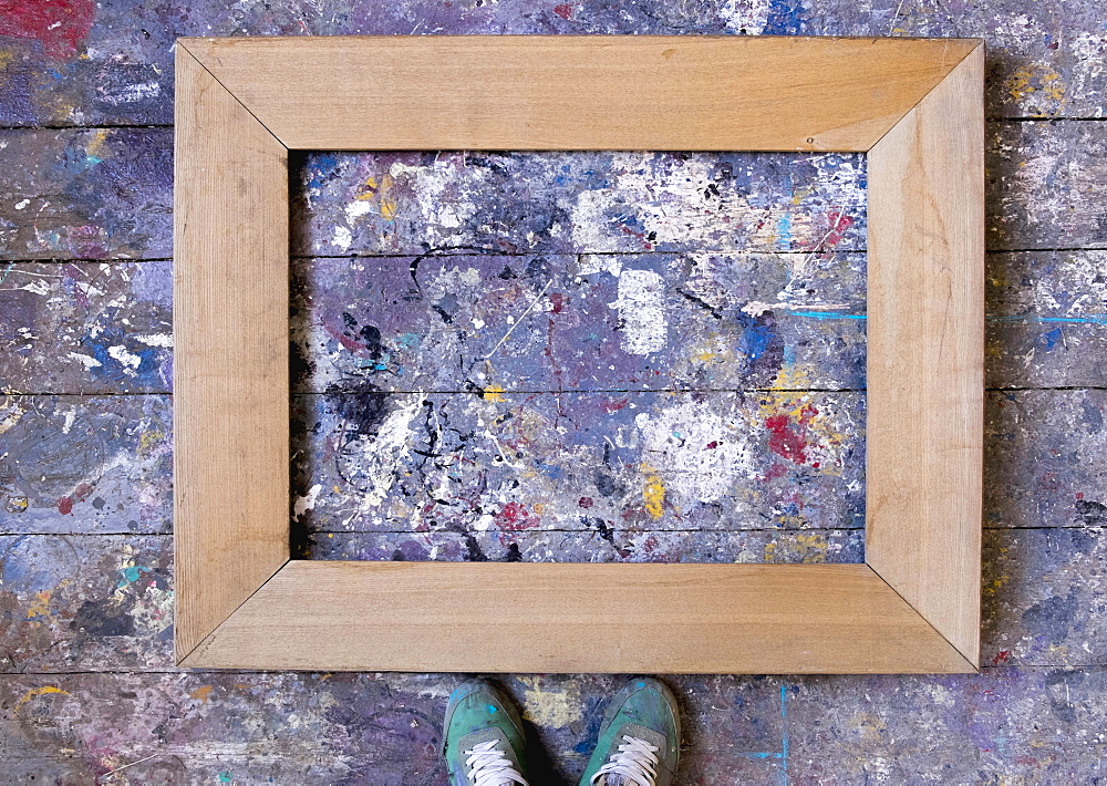 Feet standing over picture frame on wooden floor