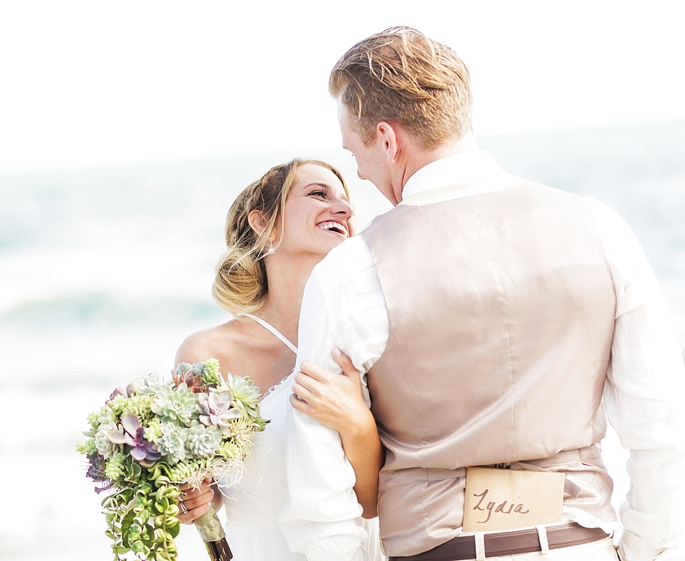 Caucasian bride and groom hugging on beach