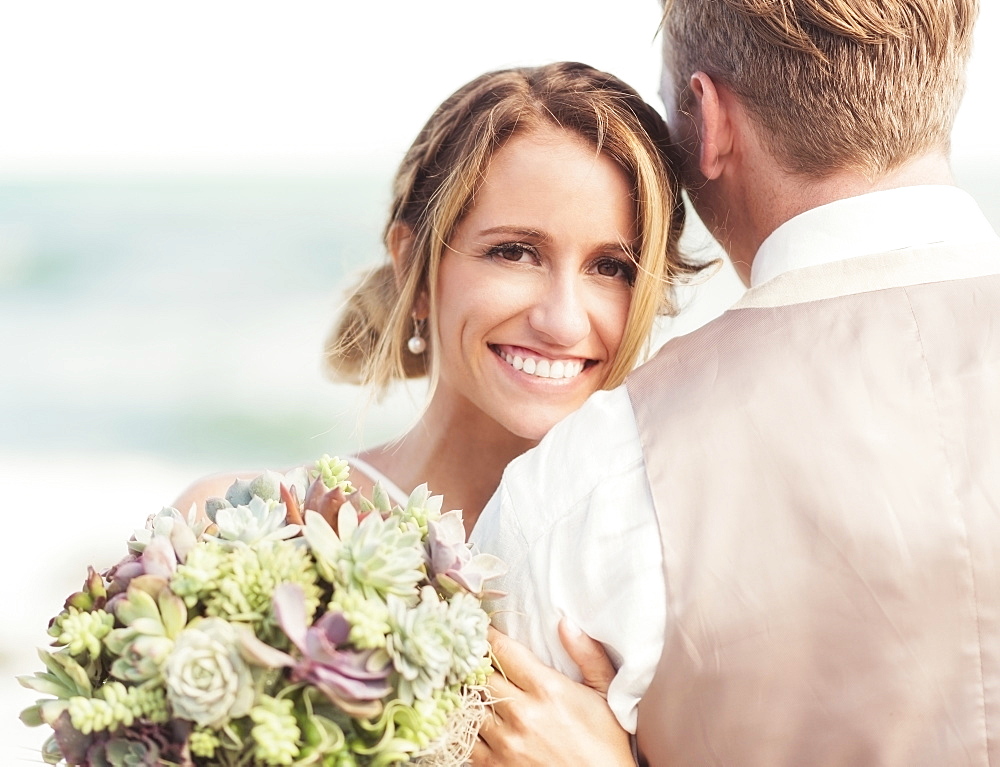 Caucasian bride and groom hugging on beach