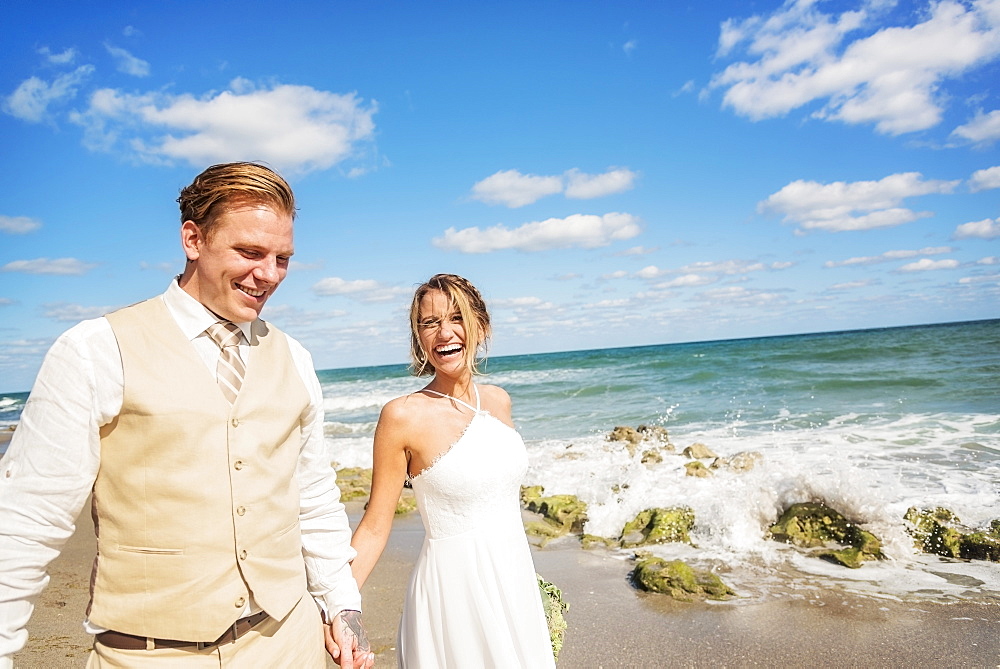 Caucasian bride and groom holding hands on beach