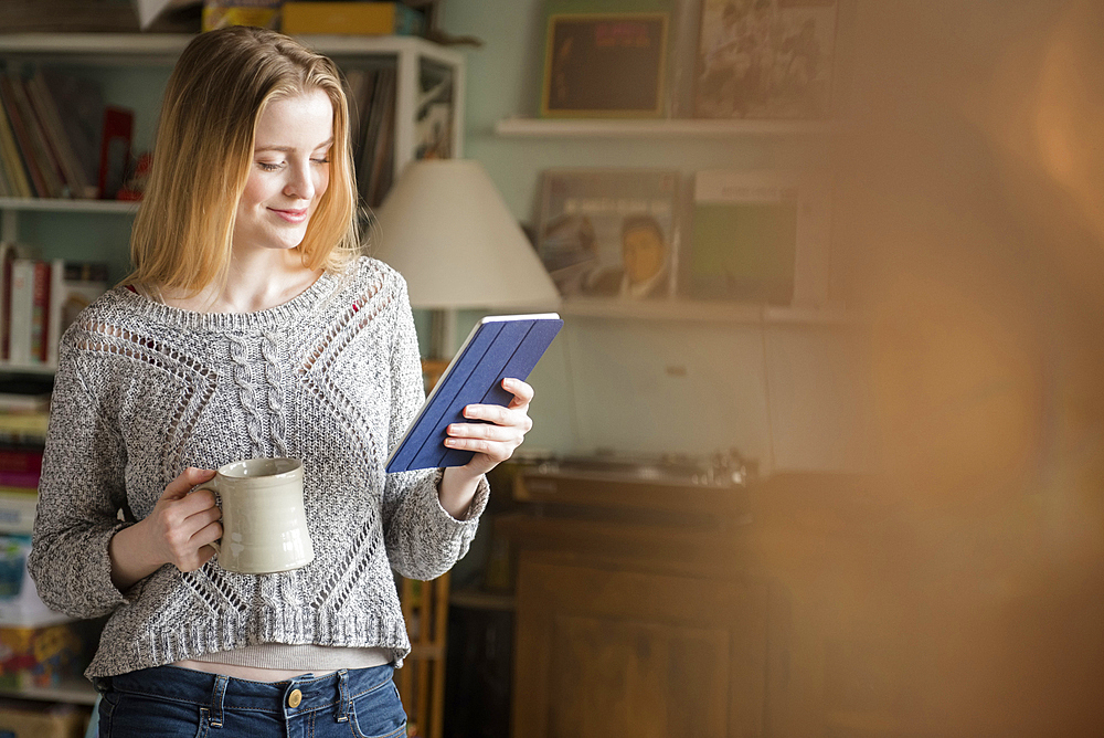 Smiling woman drinking coffee and using digital tablet