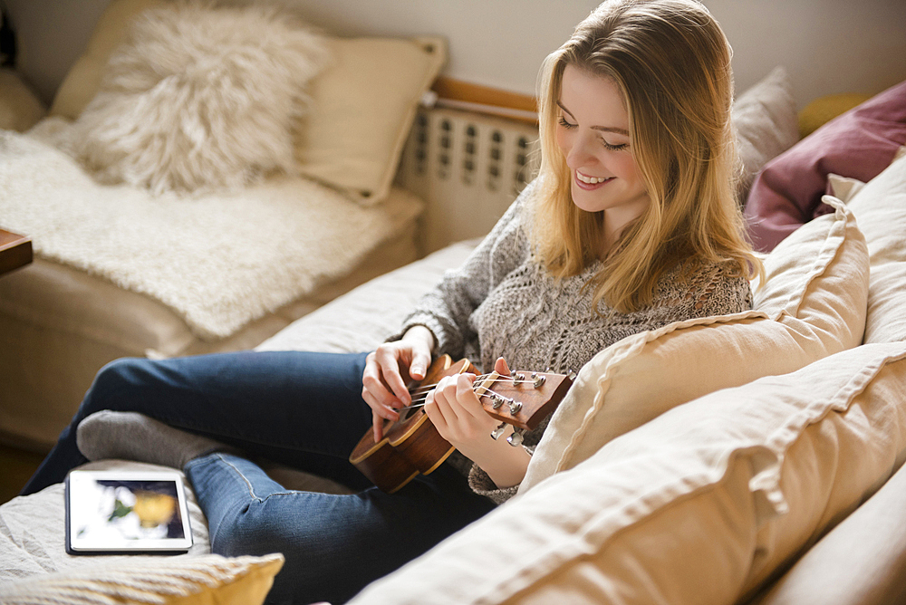 Smiling woman sitting on sofa playing ukulele