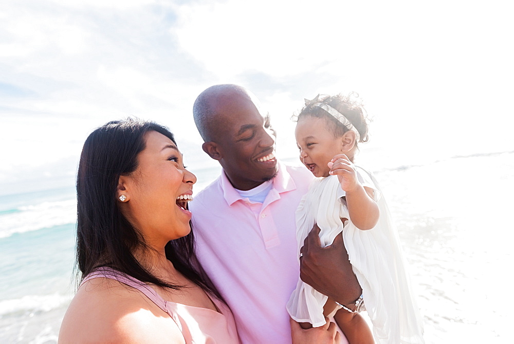 Couple laughing with baby daughter near ocean