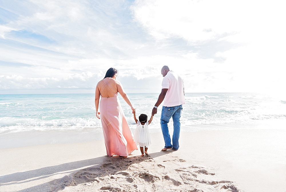 Couple holding hands of baby daughter walking on beach