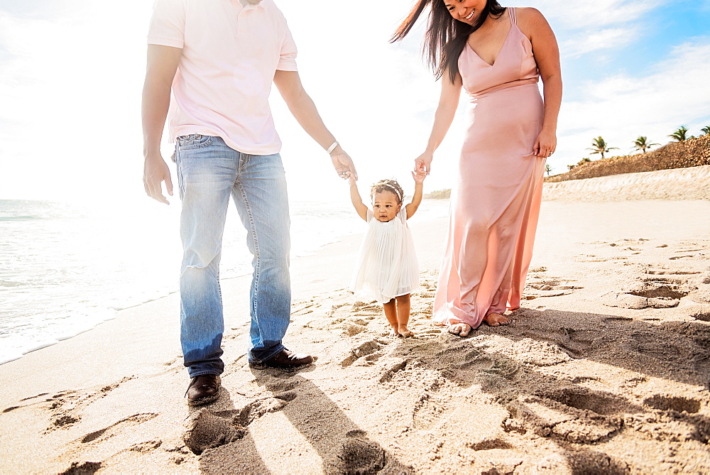 Couple holding hands of baby daughter walking on beach