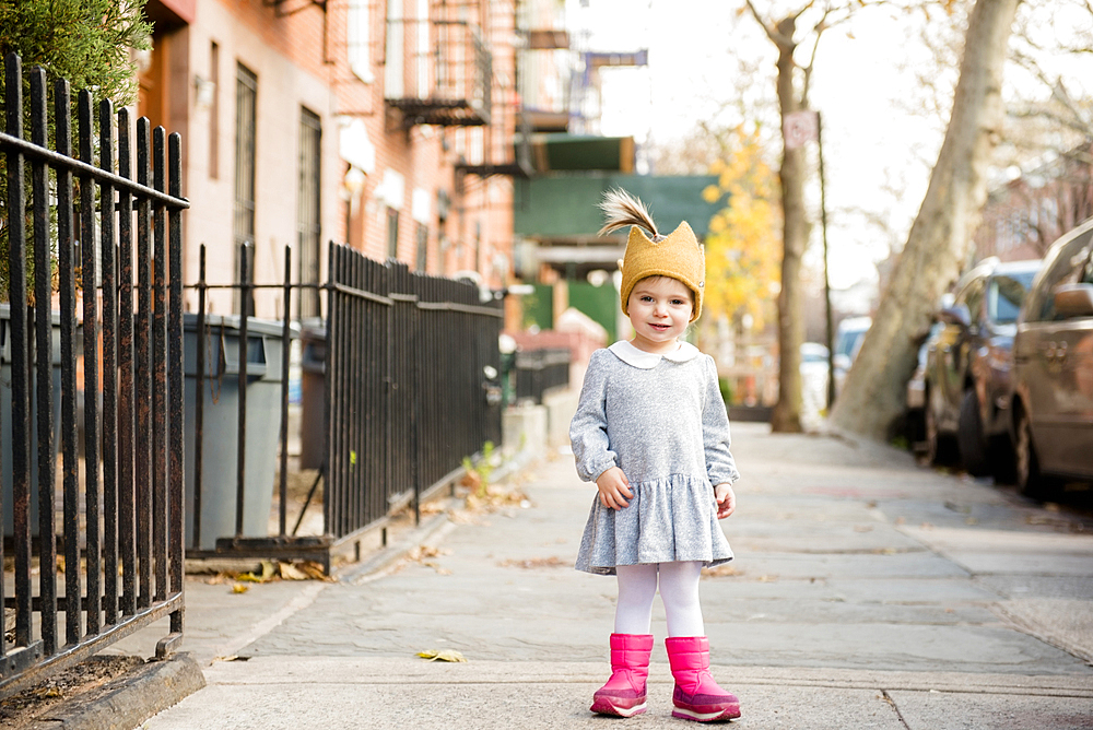 Smiling Caucasian baby girl wearing crown hat on city sidewalk