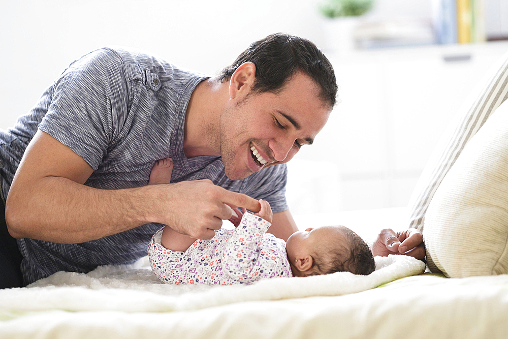 Hispanic father laying on bed playing with baby daughter