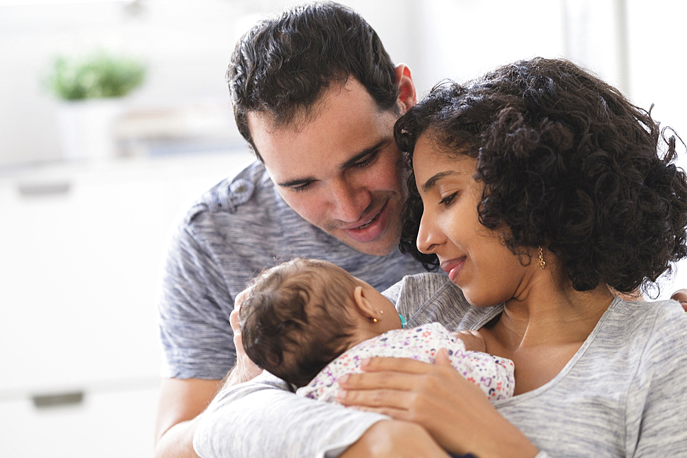 Hispanic mother and father admiring baby daughter