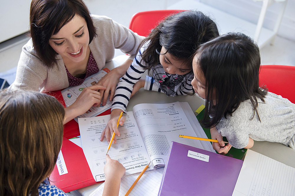 Teacher helping girls with workbook in classroom