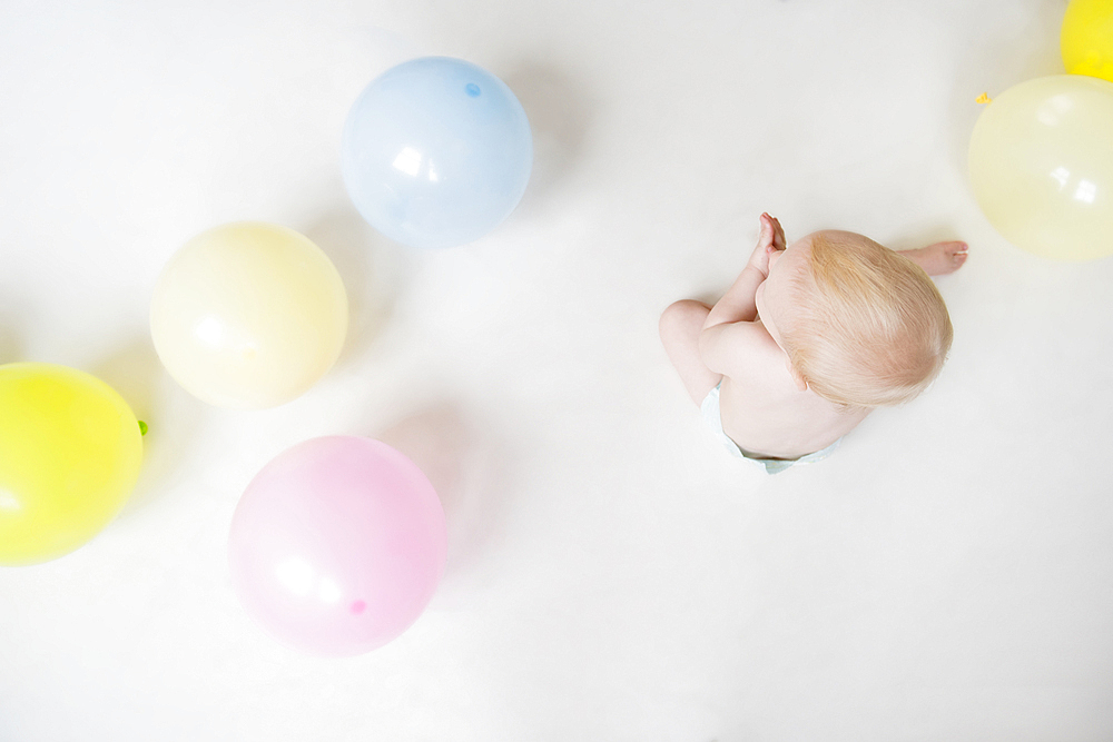 Caucasian baby boy sitting on floor with balloons