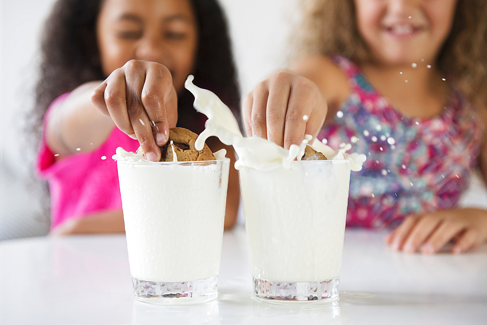 Girls splashing cookies in glasses of milk