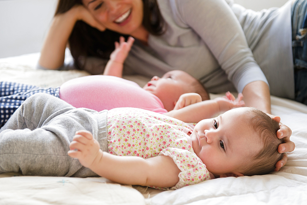 Caucasian mother caressing head of baby daughter on bed