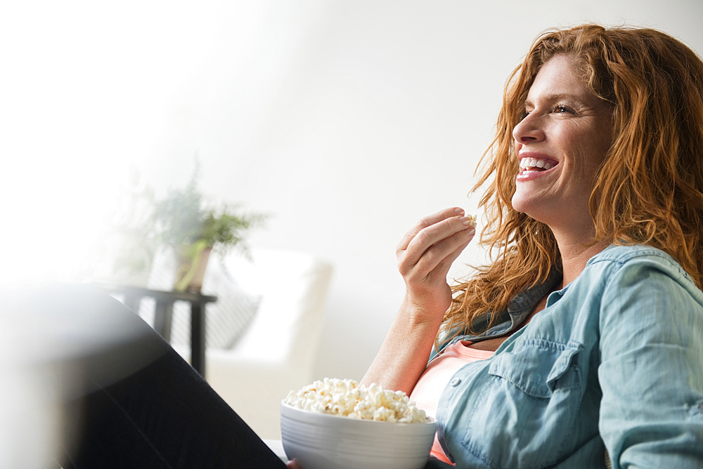 Laughing Caucasian woman eating bowl of popcorn