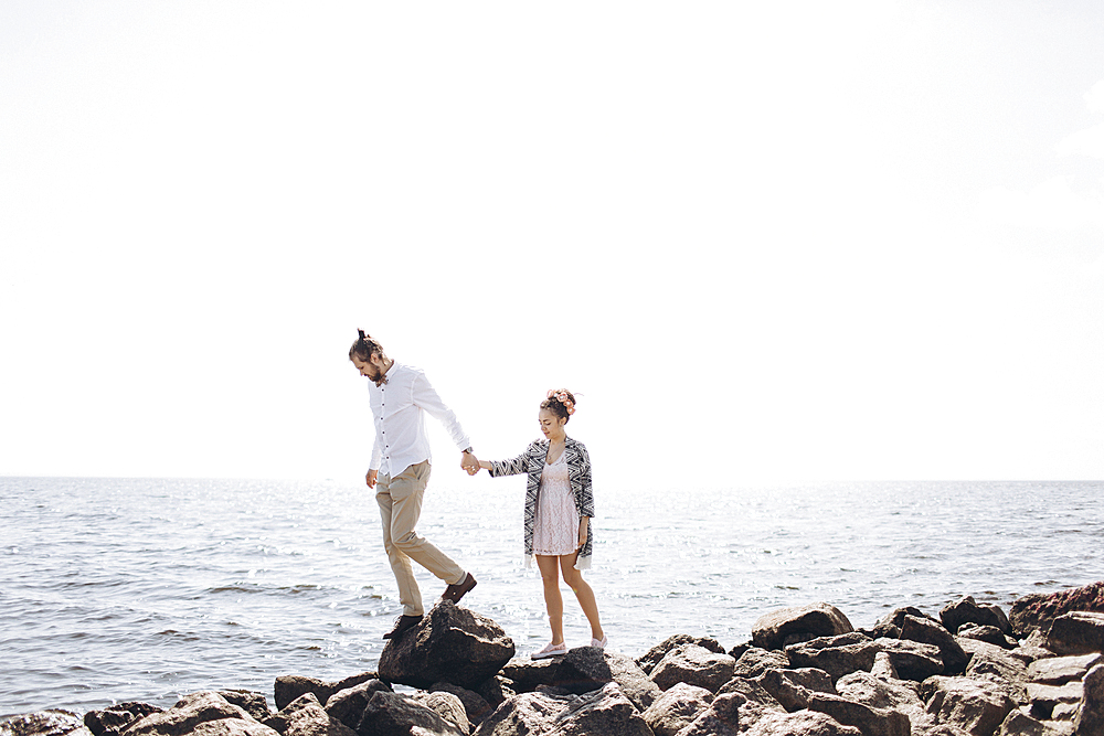 Middle Eastern couple walking on rocks near ocean