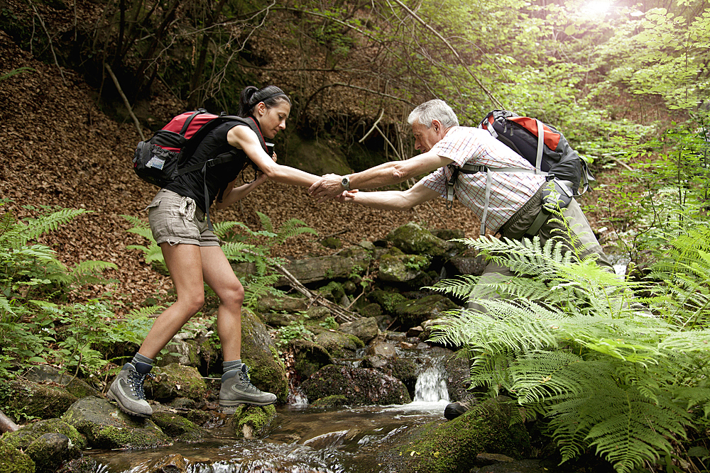 Caucasian man helping woman crossing forest river