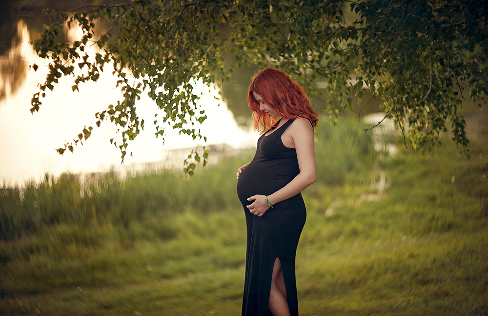 Caucasian expectant mother holding belly under tree branches