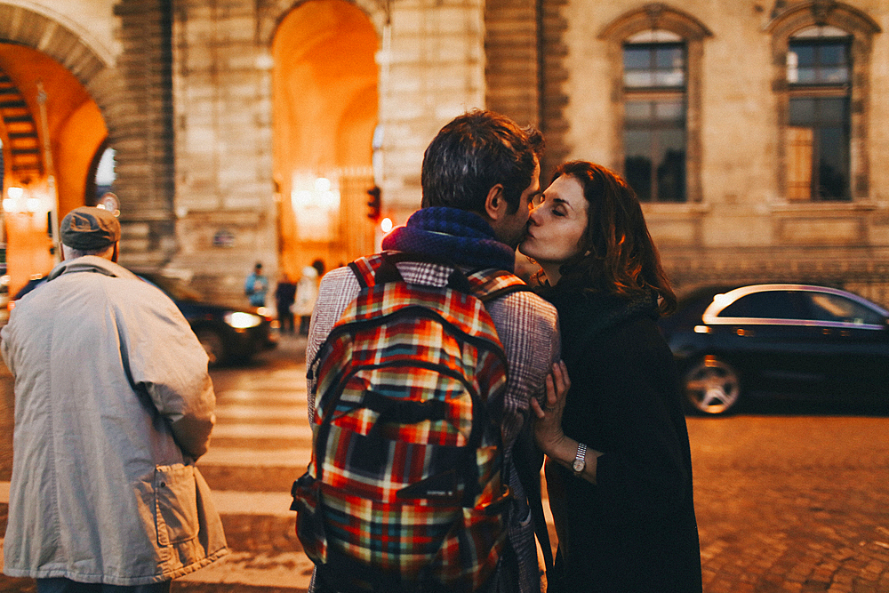 Caucasian woman kissing man on cheek in city at night