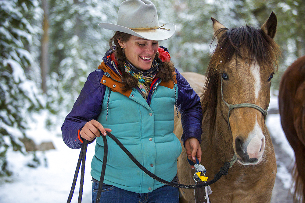 Smiling Caucasian woman holding rein of horse in winter