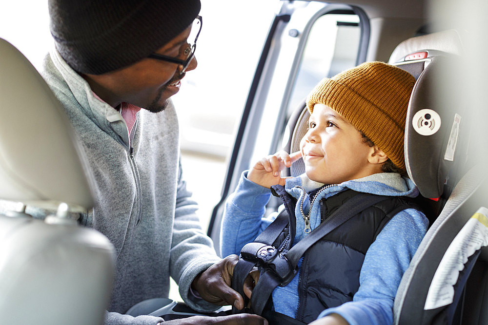 Father buckling son in car seat