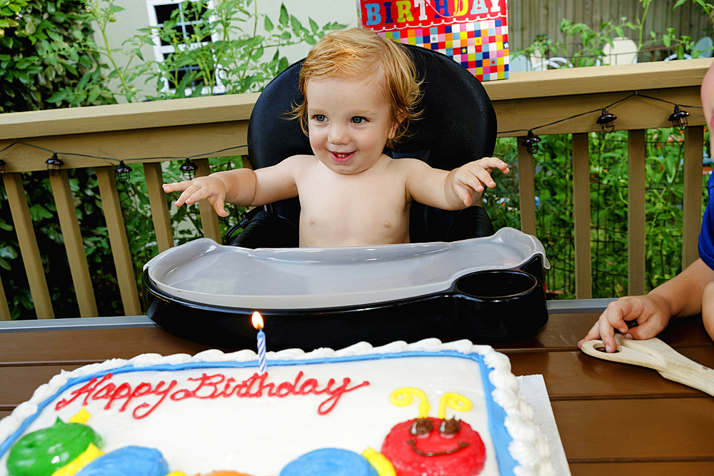 Caucasian baby boy in high chair near birthday cake