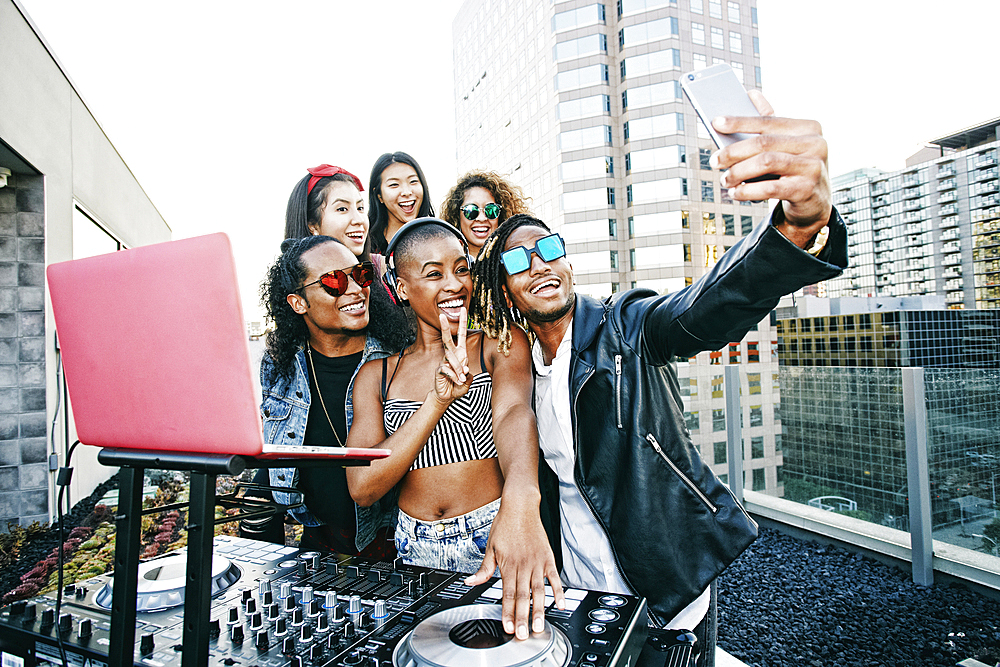 Friends posing for cell phone selfie with DJ on urban rooftop