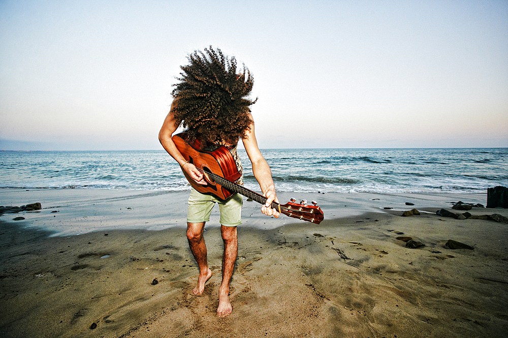 Mixed Race man tossing hair and playing guitar at beach