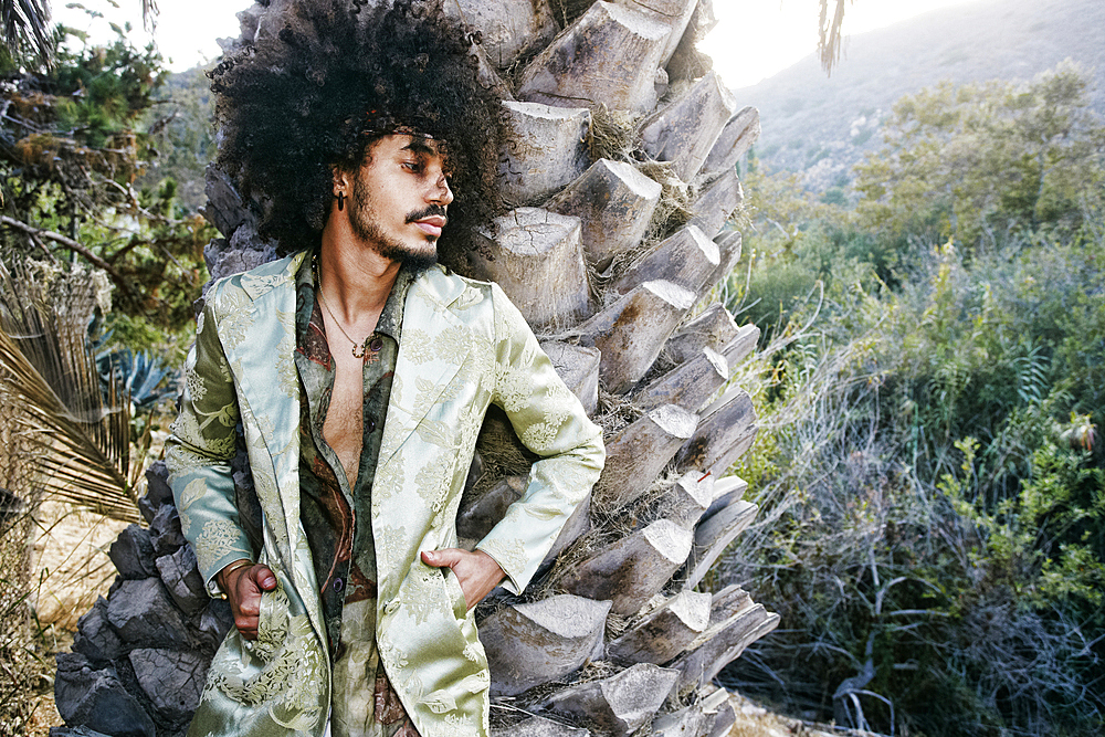 Mixed Race man wearing jacket leaning on tree trunk