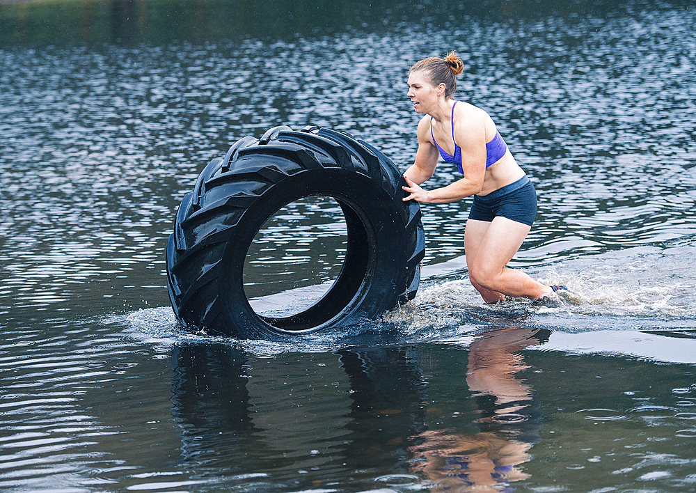 Caucasian woman pushing heavy tire in lake