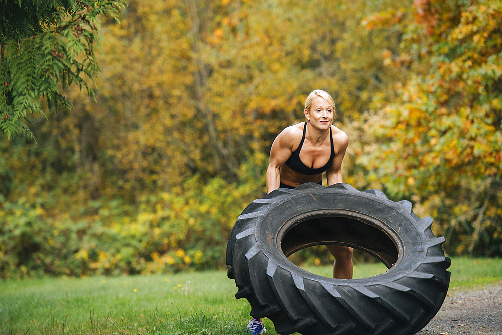 Caucasian woman lifting heavy tire in park