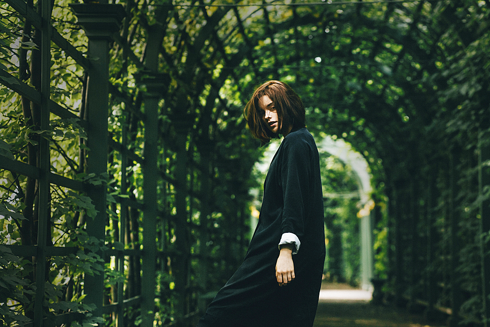 Caucasian woman wearing black dress under foliage