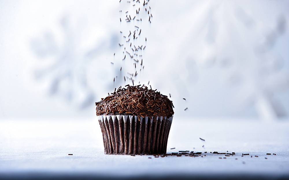 Brown sprinkles falling on chocolate cupcake