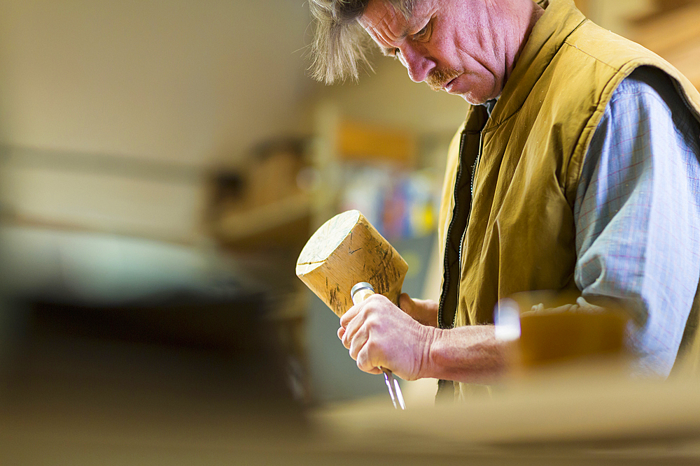 Caucasian carpenter using mallet and chisel in workshop