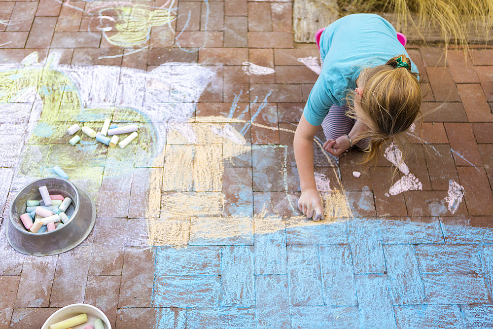 Caucasian girl drawing with chalk on patio bricks