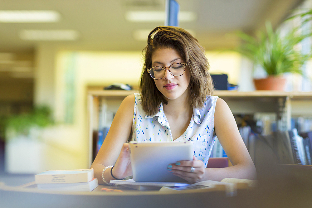 Mixed Race girl reading digital tablet in library