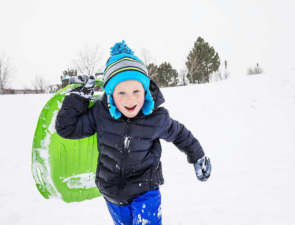 Smiling boy running with toboggan in winter