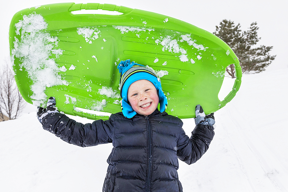 Smiling boy posing with toboggan in winter