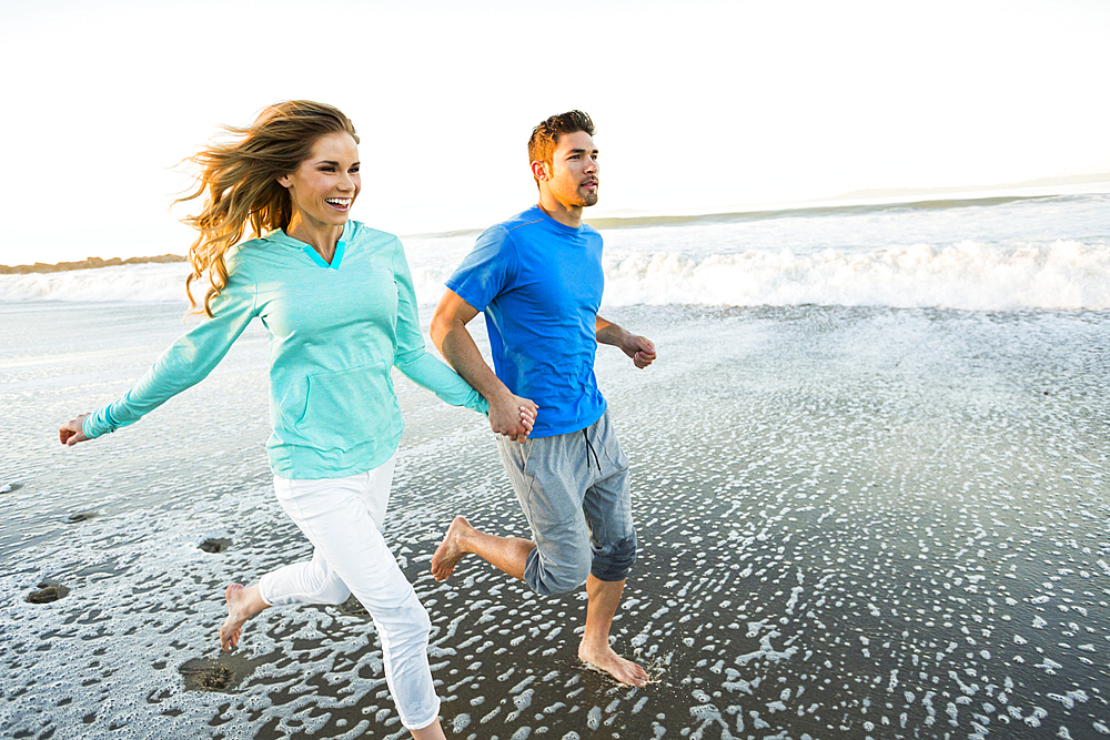 Couple holding hands running on beach