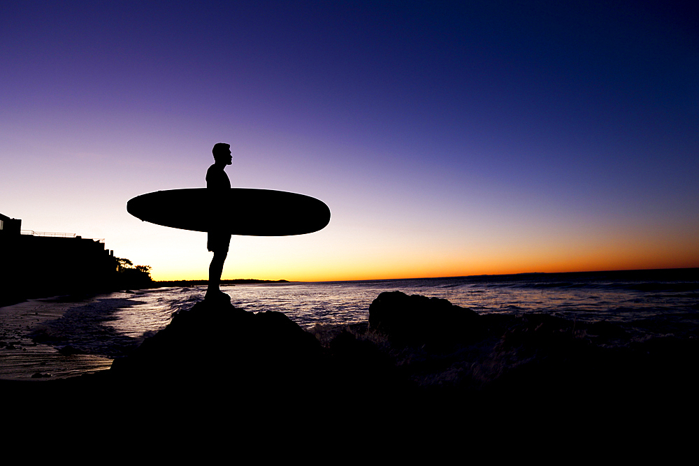 Silhouette of Hispanic man holding surfboard at beach