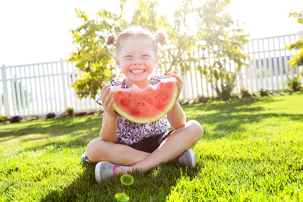 Caucasian girl sitting in grass eating watermelon