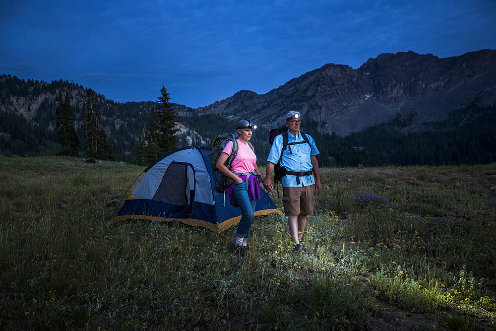 Caucasian couple wearing headlamps at mountain campsite