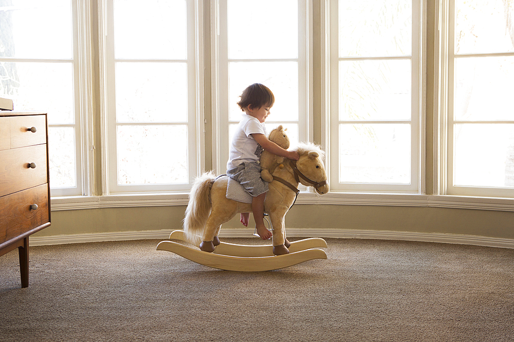 Mixed Race boy sitting on rocking horse near window