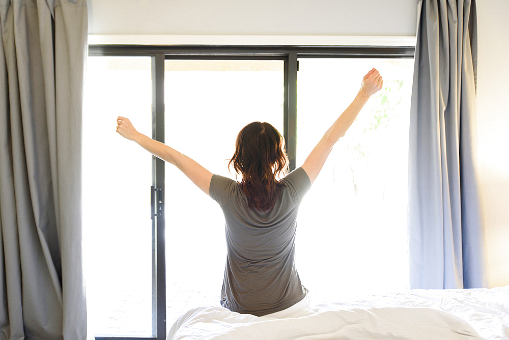 Caucasian woman sitting on bed stretching arms