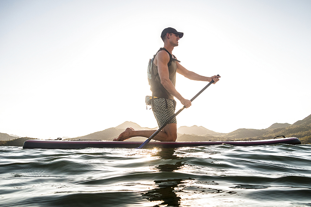 Caucasian man kneeling on paddleboard in river