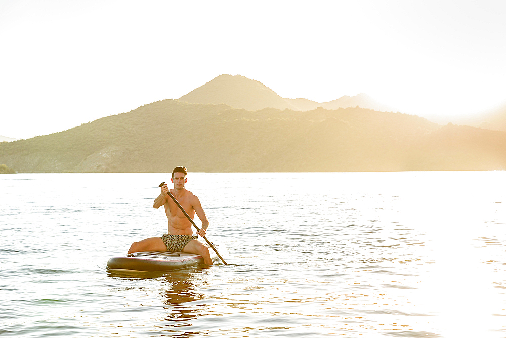 Caucasian man sitting on paddleboard in river